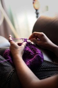 Woman knitting prayers into a purple scarf