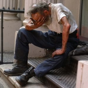 An overwhelmed homeless man sitting on front stoop, resting his head on his knees.