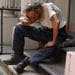 An overwhelmed homeless man sitting on front stoop, resting his head on his knees.