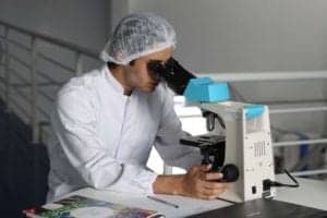 A lab technician looks in a microscope before confirming a difficult diagnosis