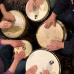 A view of five sets of hands drumming on djembe drums