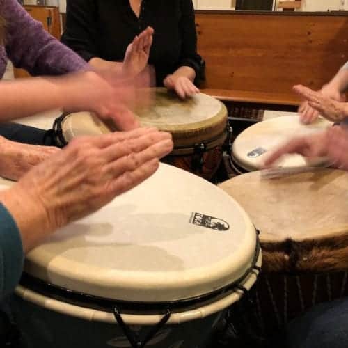 Hands in motion as they play on djembe drums gathered in a circle.