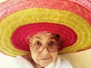 An old lady wears a colorful red and yellow striped sobrero, perhaps to celebrate aging.