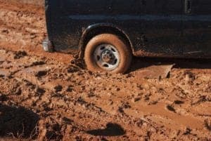 A rear wheel of a car is stuck in deep mud.