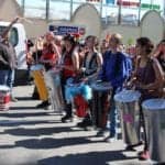 A lind of colorful drummers in native dress playing tall djembes