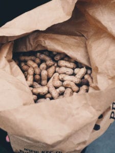 A brown paper bag full of unshelled peanuts.