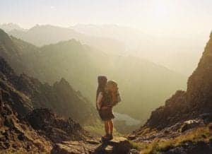 Man climbing in mountains with a heavy backpack on his back.