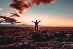 Man stands with arms uplifted facing the horizon