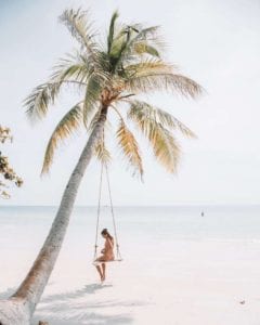 Woman on a swing under a palm tree maybe taking 'me-time" for her own self care