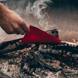 a hand putting a piece of red paper into the coals of a fire