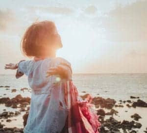 young woman celebrating a full life with hands outstretched by the sea