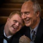 older man smiling as he hugs disabled young man