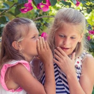 little girl listening to a friend whisper in her ear