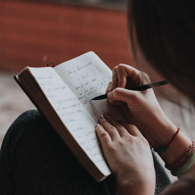 woman's hands writing in a journal, perhaps she is owndering if she is a writer