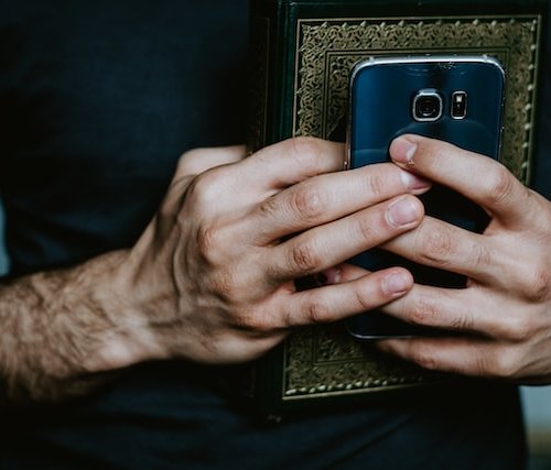 hands holding a prayer book and cell phone - technology, spirituality and religion meet