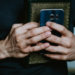 hands holding a prayer book and cell phone - technology, spirituality and religion meet